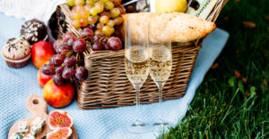 Wicker picnic basket overflowing with fresh fruit and two glasses of champagne