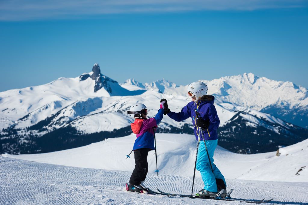 A child and parent high-five while at the summit of a ski hill at Whistler Blackcomb