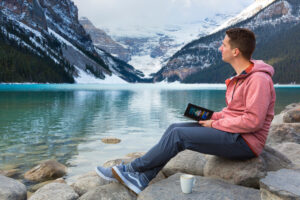 A man sitting on the rocks, journaling, on the shores of Lake Louise. Wellness at Fairmont Chateau Lake Louise.