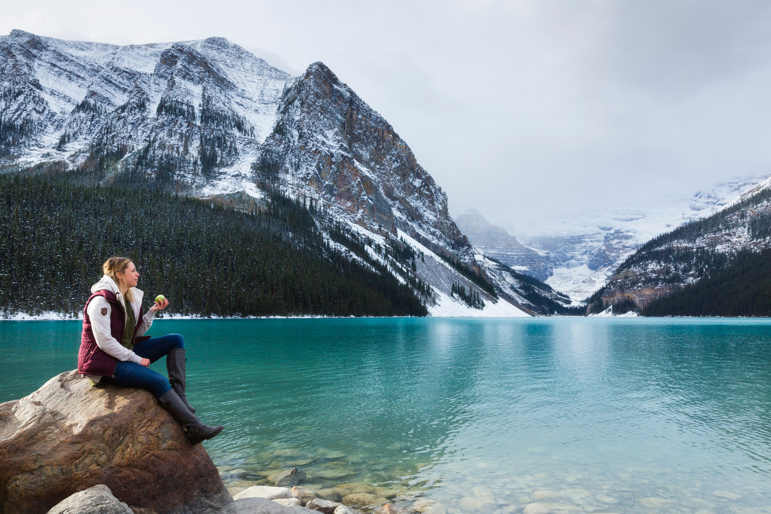 A Woman sitting on a rock on the shores of Lake Louise. Nick-Fitzhardinge