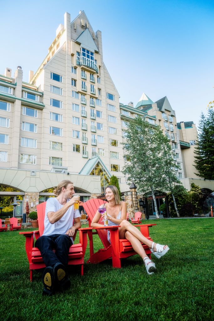 A couple enjoying drinks outside in Adirondack chairs at Fairmont Chateau Whistler