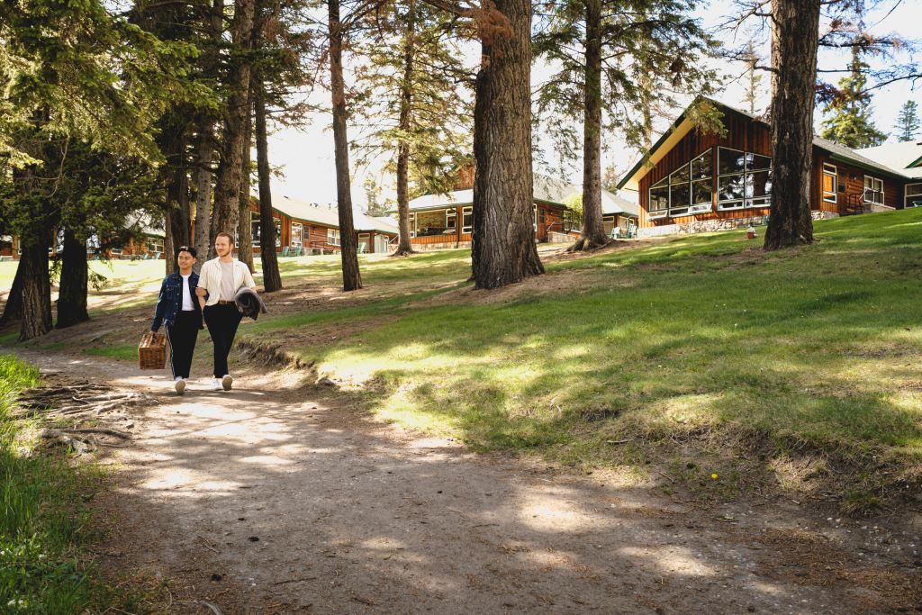 A couple walking with a picnic basket through Fairmont Jasper Park Lodge in summer