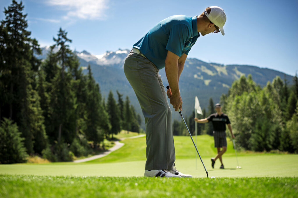 Man putting towards friend with flag  in Whistler at the Fairmont Chateau Whistler Golf Club